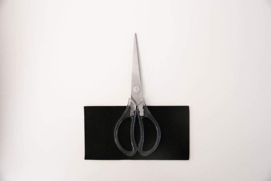 Sharp metal scissors placed on a black surface, captured from above on a white background.